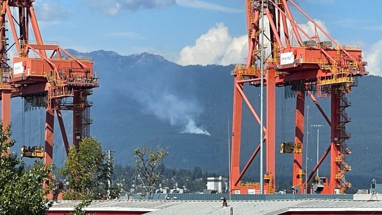 A wildfire is pictured burning on hills between two large port loaders.