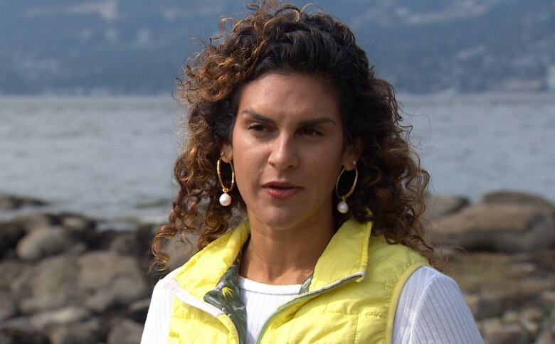 A woman with long curly hair in a yellow vest.