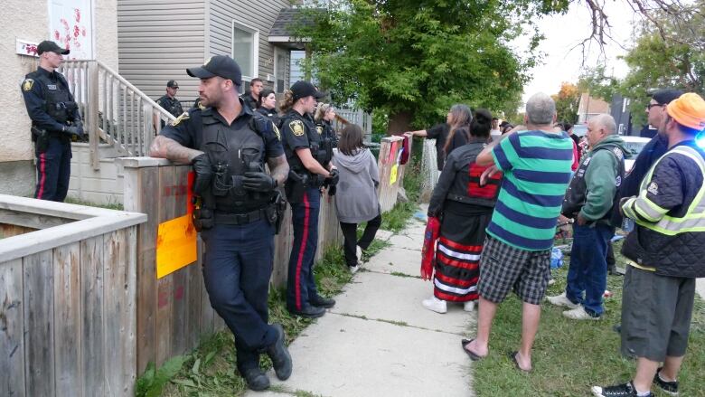 Police officers stand between a group of protesters and a house.