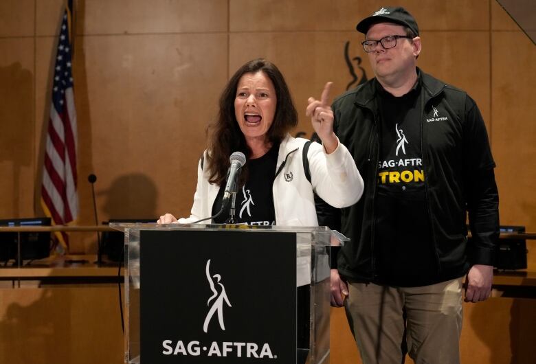 A woman gives an impassioned speech at a podium, with a colleague flanking her to her  left.