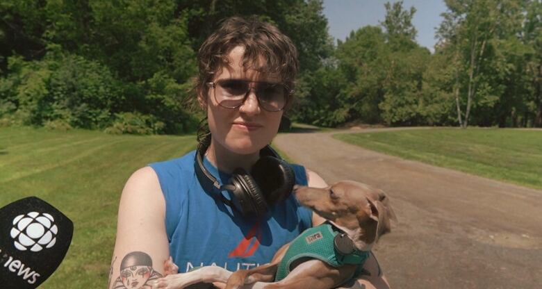 A person wears headphones around their neck and holds a small dog in their arms.