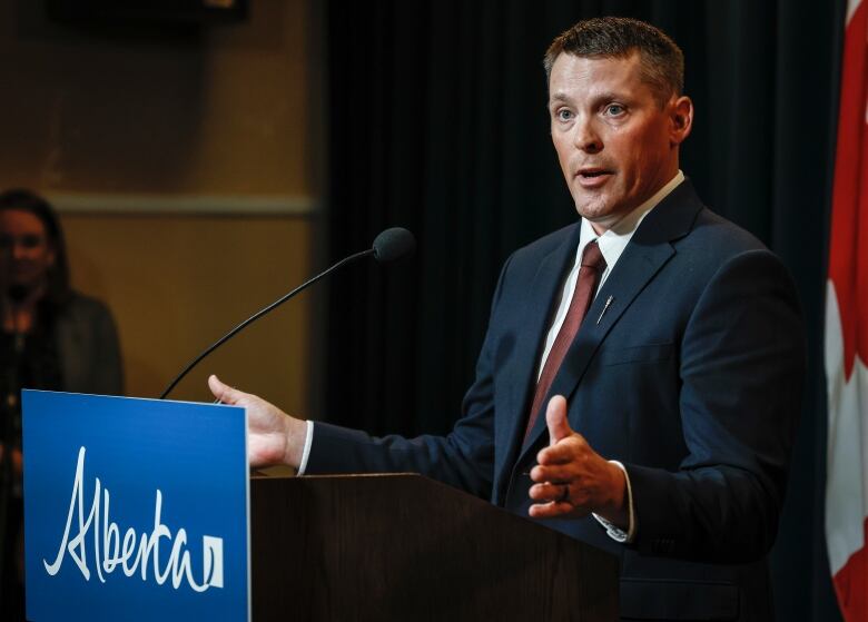 A man standing at a podium with arms outstretched. 