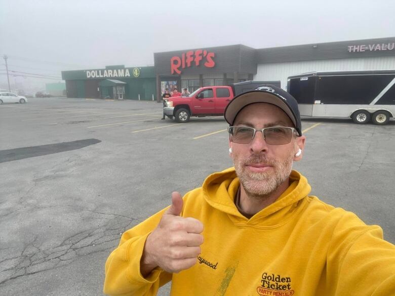 A man wearing a yellow sweater standing in a parking lot. 