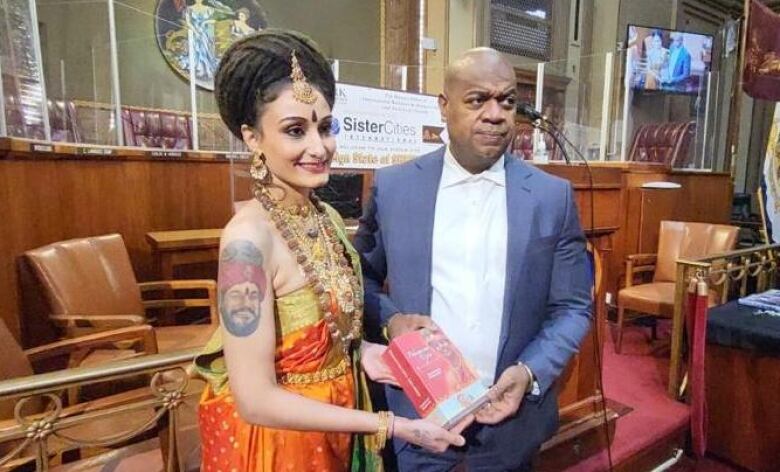 A woman dressed in Indian attire is presenting a gift to a man in a suit. 