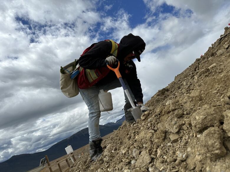 A man bends to plant a tree on a rocky hillside.