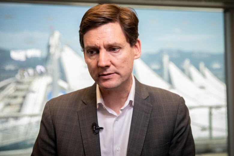 A white man in a white shirt and grey suit looks solemn during an interview.