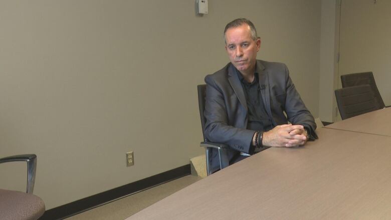 Bill Marra sits at a table with his hands interlocked