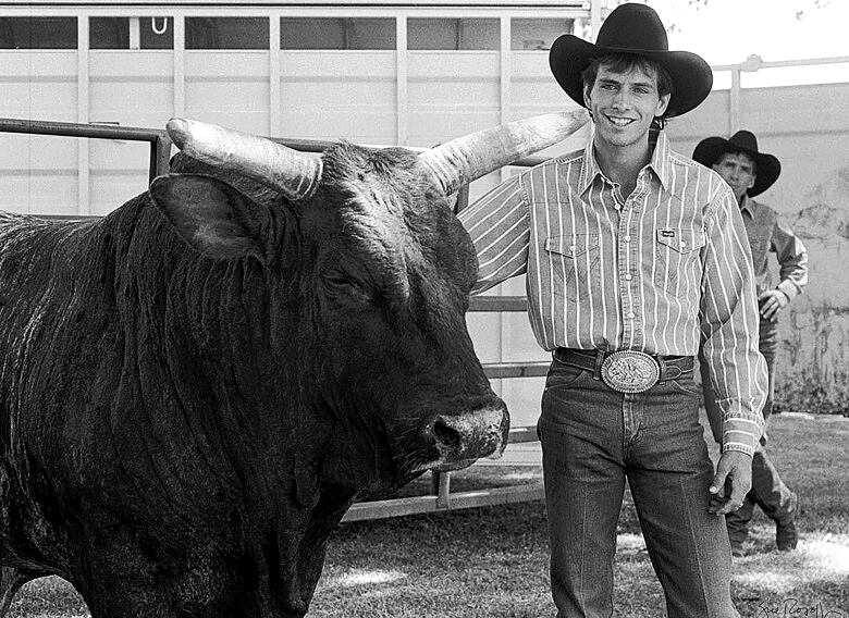 A black and white image of a man with a bull is pictured.