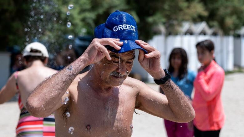 A man fills a baseball hat with water and pours it over his head.