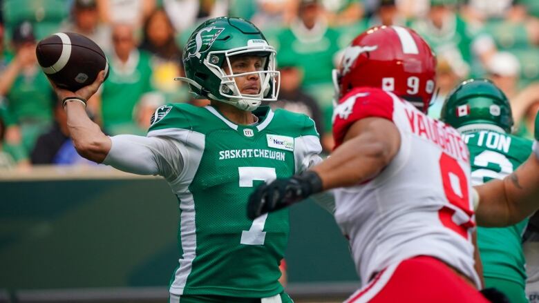 A green jerseyed quarterback prepares to throw a football with a white jerseyed defender approaching