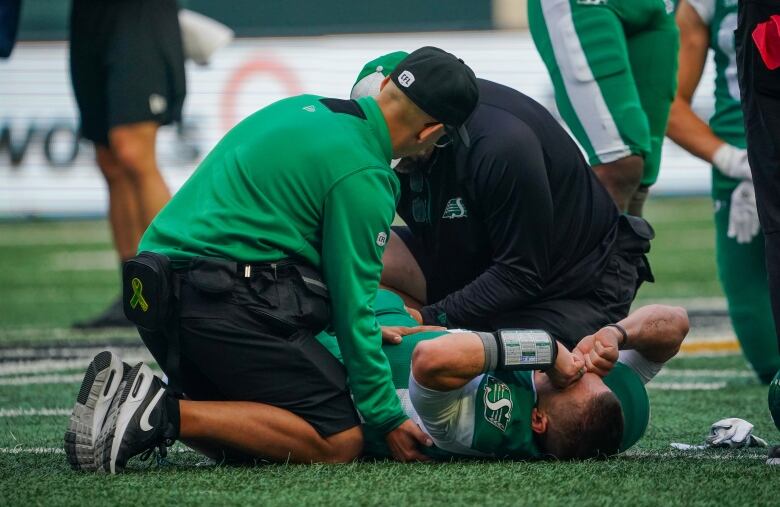 Two people hover over an injured man in a green jersey