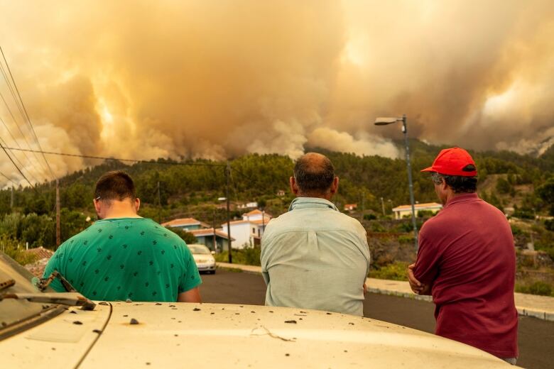 People watch a wildfire on a hill, close to homes.