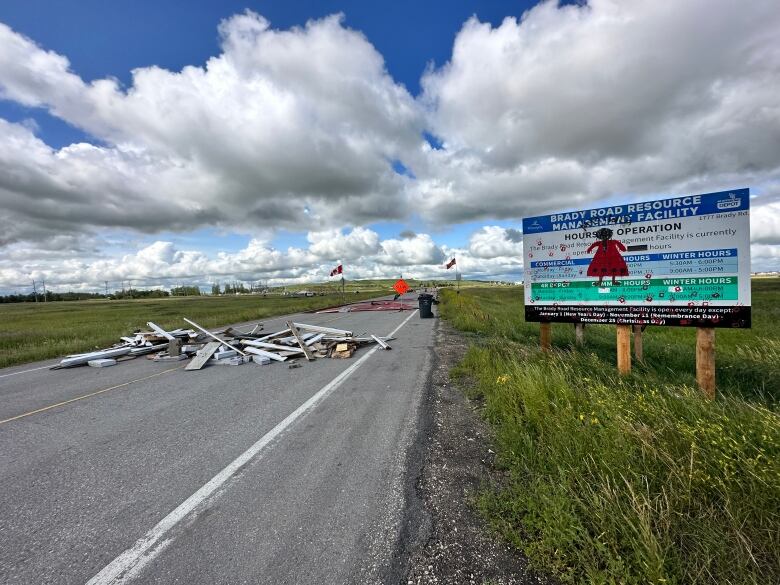 A pile of wood sits on a road. A woman in a red dress is painted on a sign next to the road.