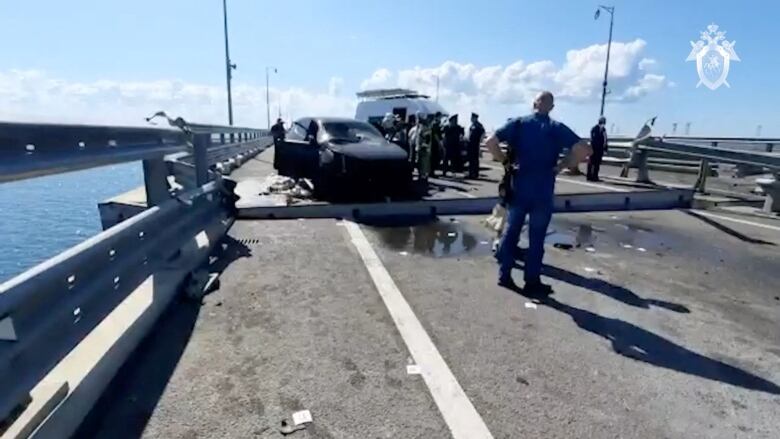 Several people and a vehicle are shown on a damaged bridge.