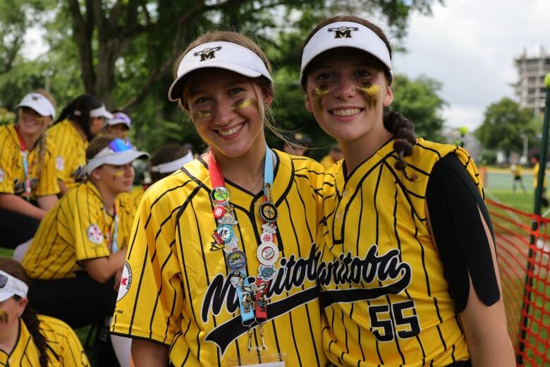 Two girls in yellow uniforms stand close to each other, one with a variety of pins on a lanyard around her neck.