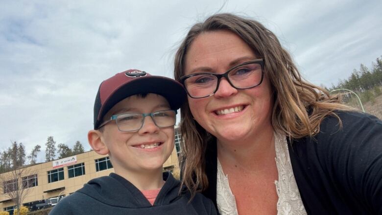 A white mother and son, both with glasses and brown hair, pose together for a selfie on a cloudy day.