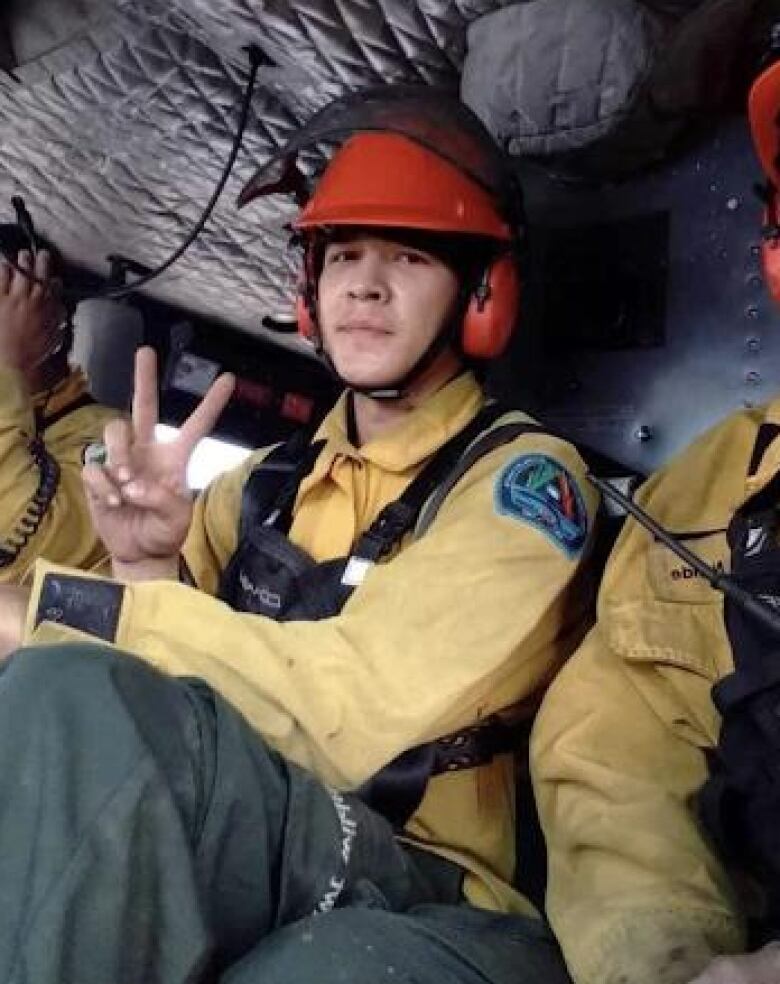 A young man in a helmet sitting inside an aircraft gives the peace sign.