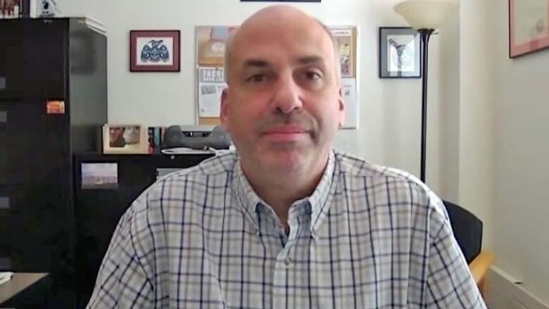 A man sitting in an office, wearing a plaid shirt.