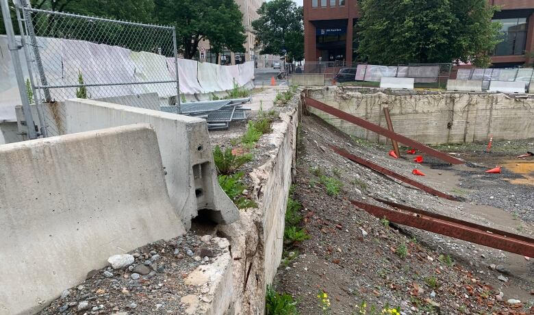 A giant hole at a city street corner with large metal beams bracing concrete walls around the perimetre. 