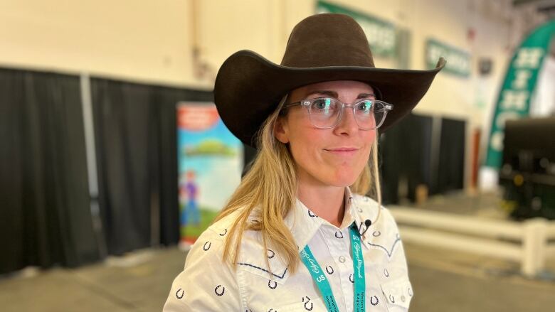 A woman in a cowboy hat and white button down poses for a picture at the Calgary Stampede.