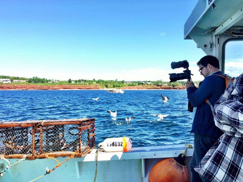 A man holds a camera while standing on a boat.