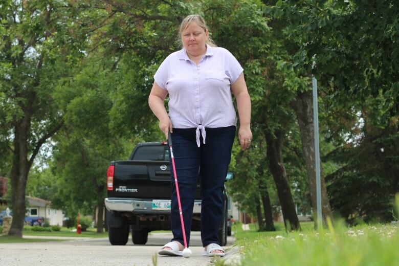 A woman used a cane to navigate walking down a road. 