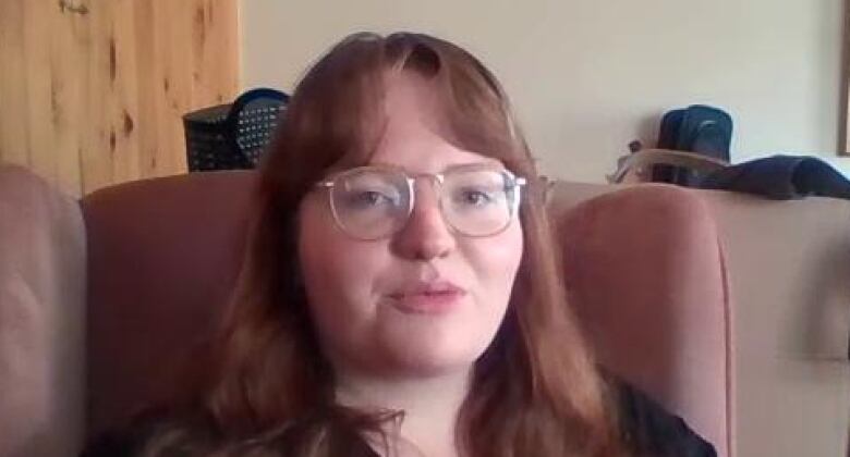 A woman with long, red hair and glasses sits on a recliner.