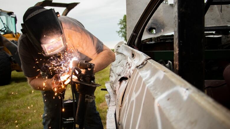 A man weld a piece of a car.