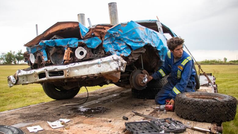 A young man fixes a beat up derby vehcile. 