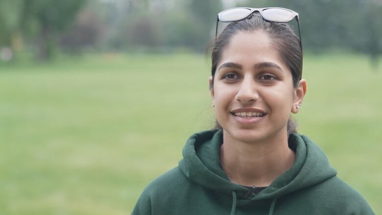 A lady in a green hoodie smiling with sunglasses at the top of her head.