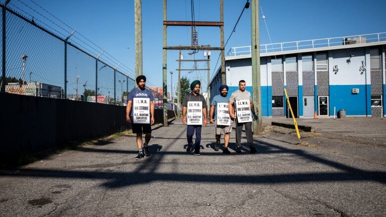 Four striking dockworkers march down an alley wearing union placards.