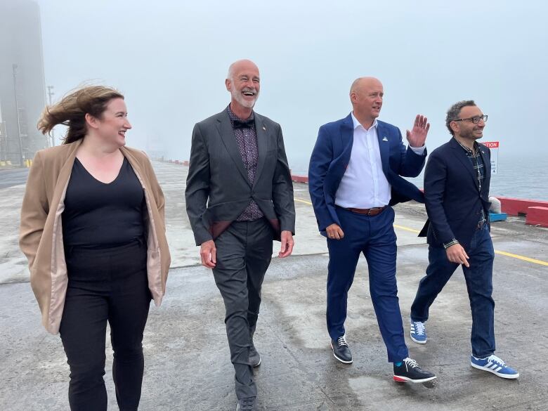 Four people walk together side by side on a dock. They are laughing and smiling.