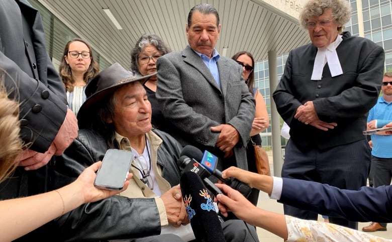 A man sitting in a wheelchair speaks to reporters. 