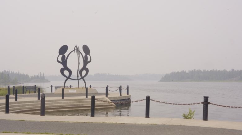 Looking out to a hazy lake, with a sculpture and steps at the lakeshore.