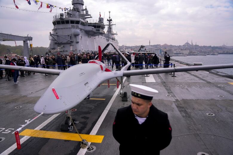 A sailor stands next to an armed drone on the deck of a naval vessel.