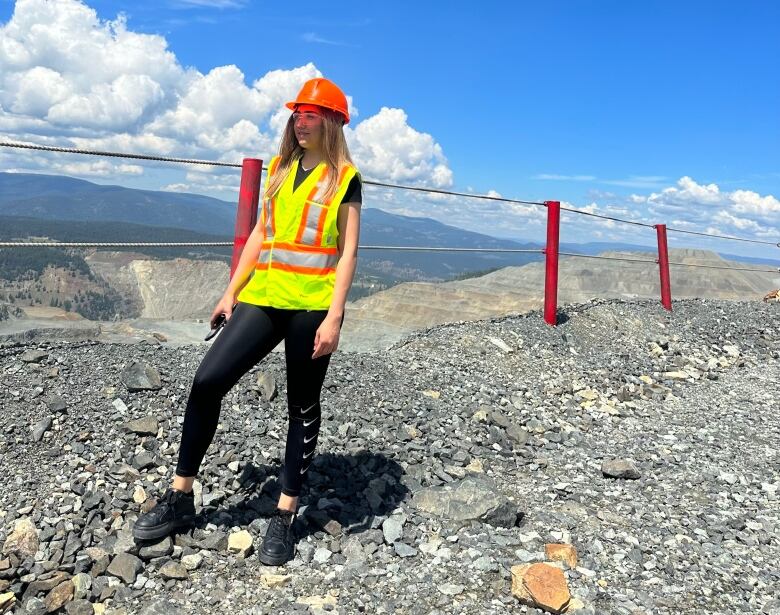 A woman in a safety vest and a hard hat looks over a cliff. 