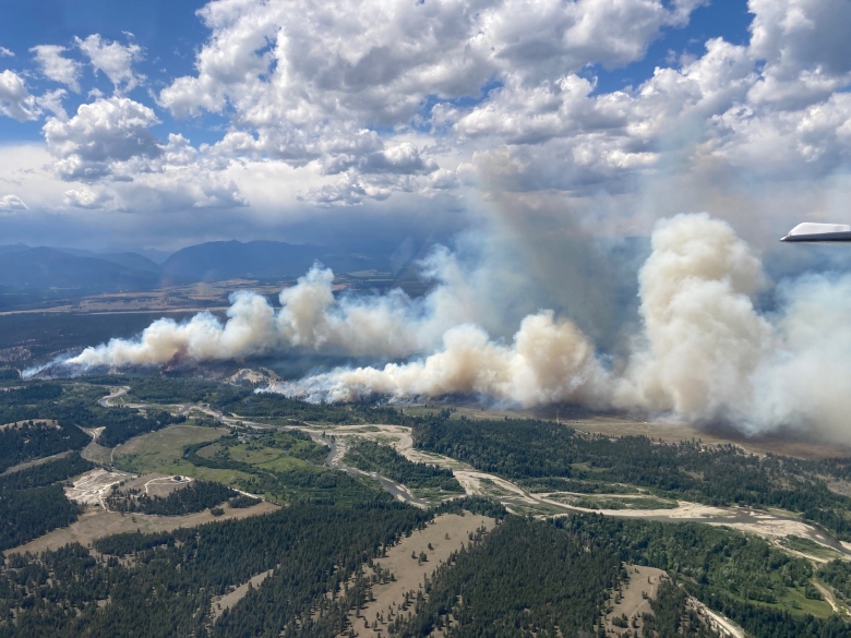 Beige wildfire smoke rises from a fire on a flat, rural area.