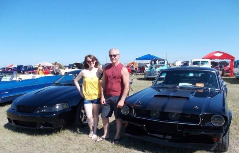 Gord and Shelby Goulding are standing next to each other in between their cars, a  1965 Ford Mustang Coupe and 2009 Shelby GT500.