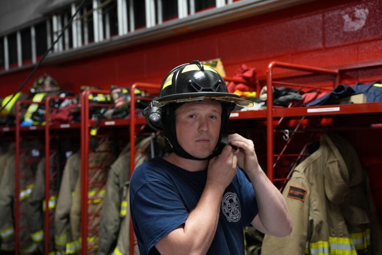 A man straps on his firefighting helmet inside a fire hall.