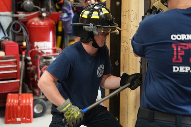 A man wearing firefighting gear attempts to open a door from the outside using a crowbar.