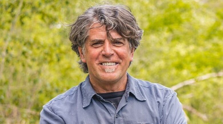 A man stands with leaves in the background. 