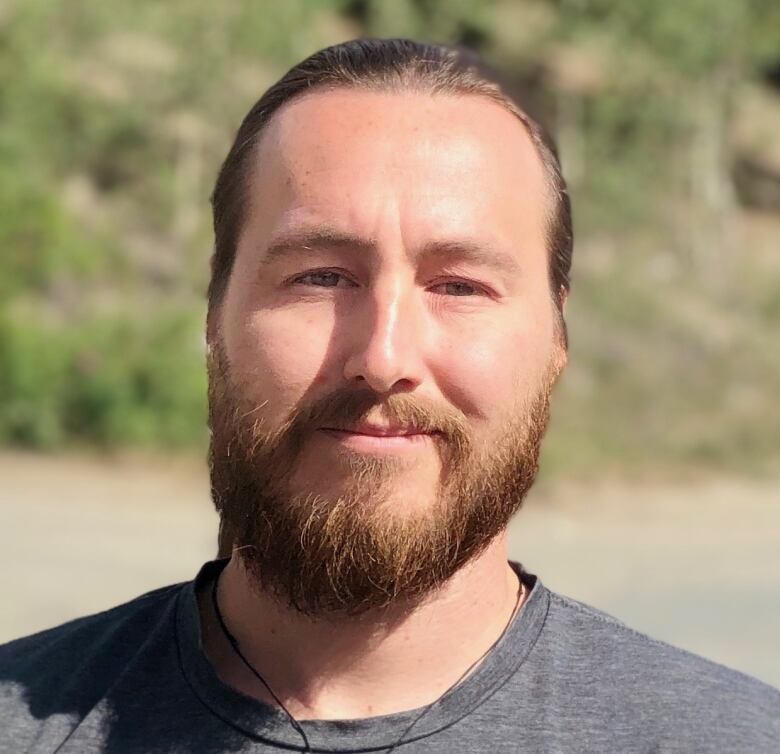 A portrait of a bearded man standing outside.