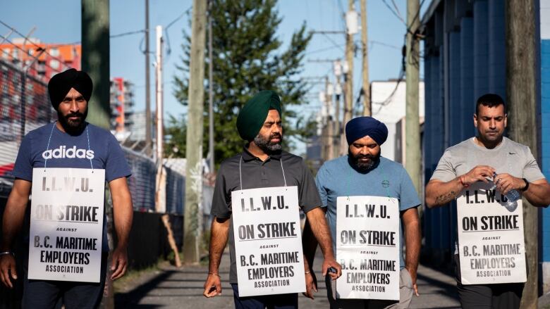 Four men wearing white sandwich boards walk down an alley on a hot day.