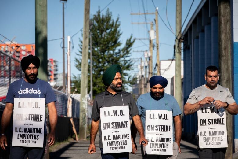 Four men wearing white sandwich boards walk down an alley on a hot day.