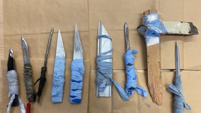 Nine handmade weapons are seen lying next to each other against a brown paper bag backdrop.