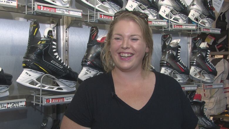 A woman with blond hair smiling in front of a wall of skates