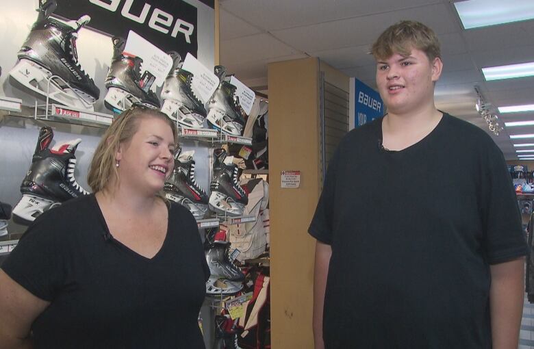 A woman smiling in front of a wall of skates, left, and a teenage boy, right, much taller than her.