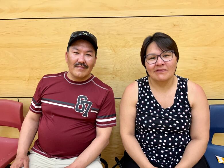 A man and a woman sit next to each other and look at the camera. 