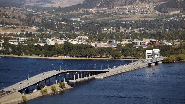 An aerial view of a bridge over a large body of water, with buildings and hills in the background.