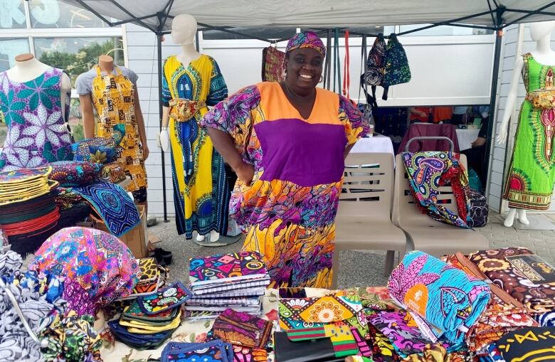 A woman smiles behind a table covered in brightly coloured clothing and cloths.